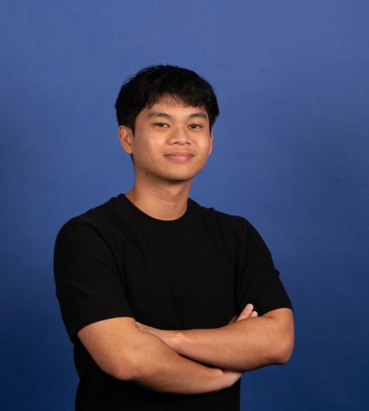 Smiling person with glasses and a mustache, wearing a plaid shirt, against a blue background.